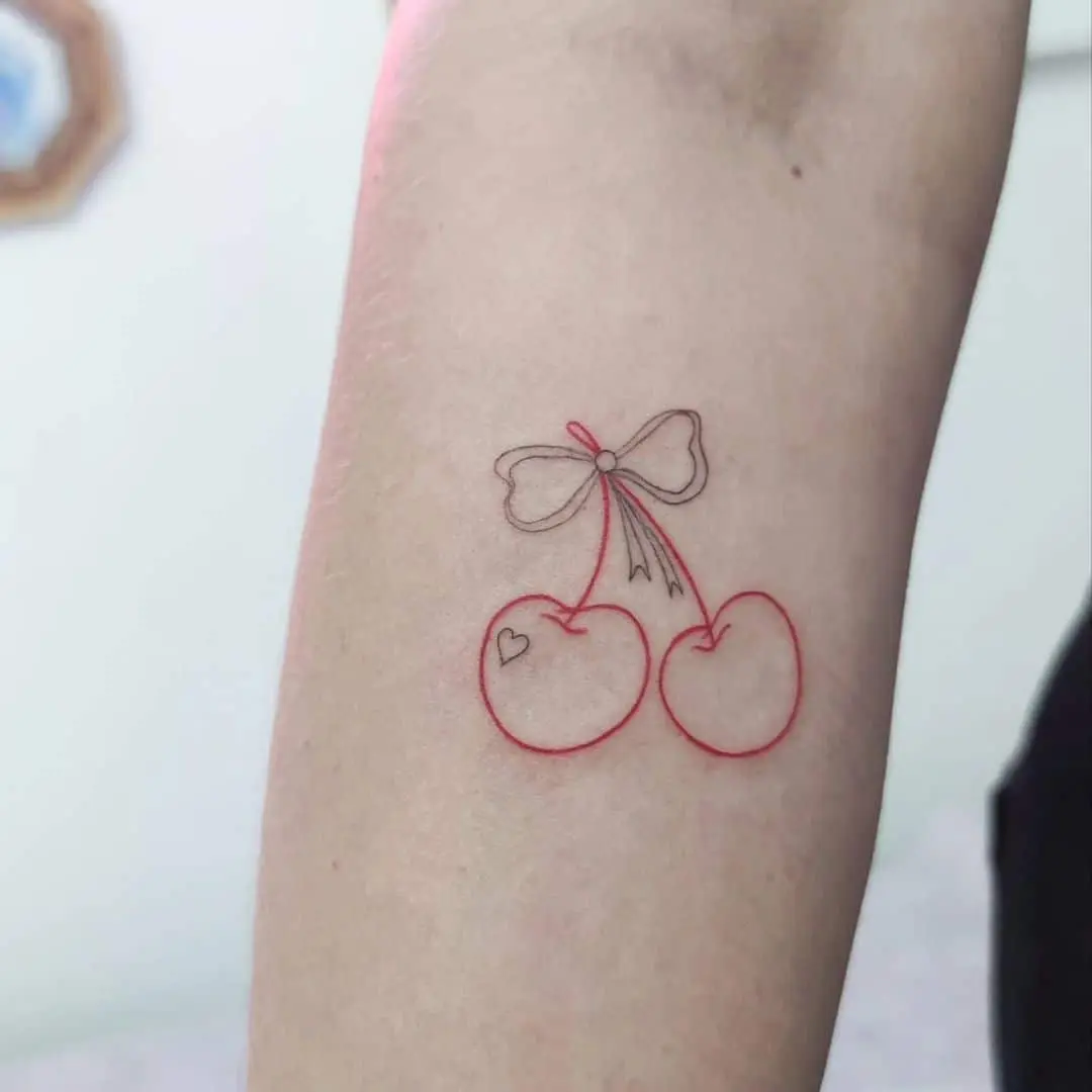 Frau mit kleinem Cherry-and-Bow-Tattoo am Unterarm